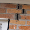 A brick wall displaying stair-step cracks and messy tuckpointing on a Lockport home